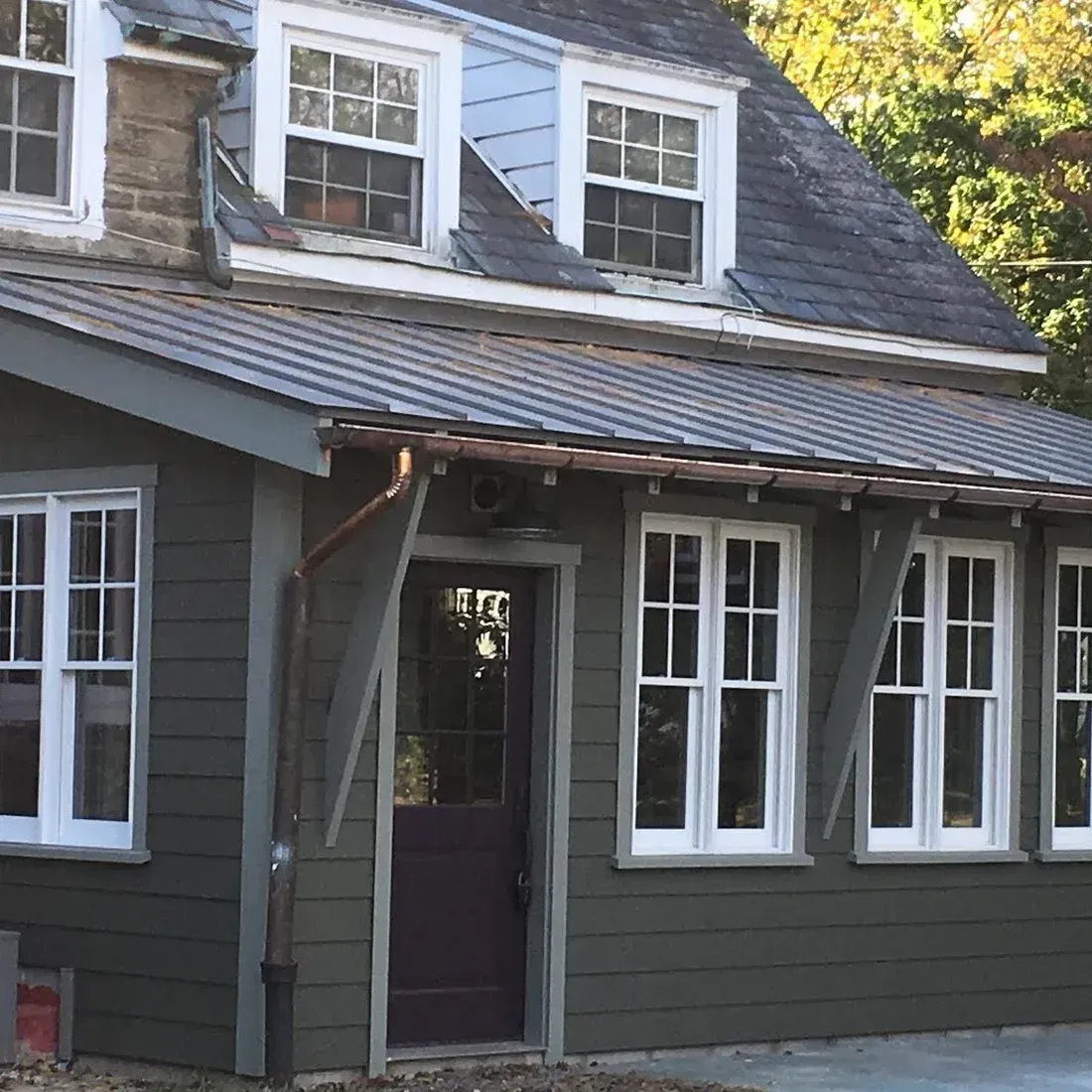 Gray house exterior with white-trimmed windows and a covered porch in sunlight
